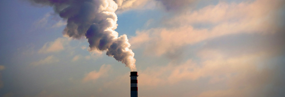 A chimney emitting a thick plume of white smoke in front of a cloudy blue sky